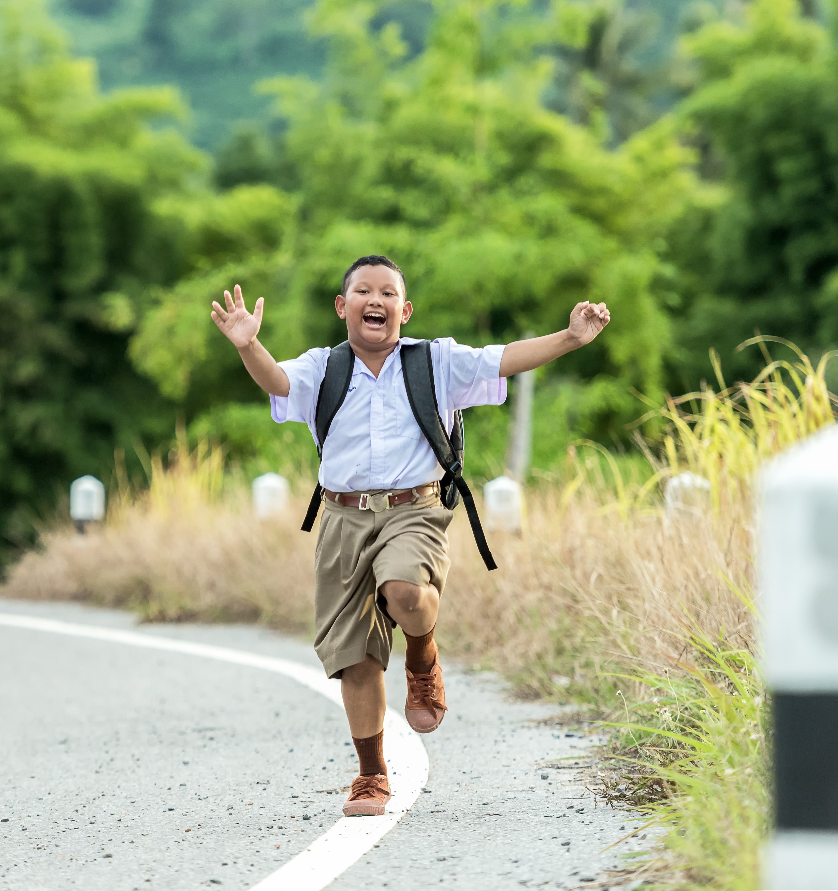 little boy joyfully running down the edge of the road in school uniform